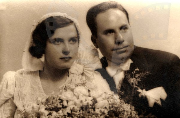 Ein Schwarz-Weiß-Foto eines strahlenden Mannes und einer Frau an ihrem Hochzeitstag, die Frau in einem weißen Kleid mit einem Strauß Blumen in der Hand, der Mann steht neben ihr.