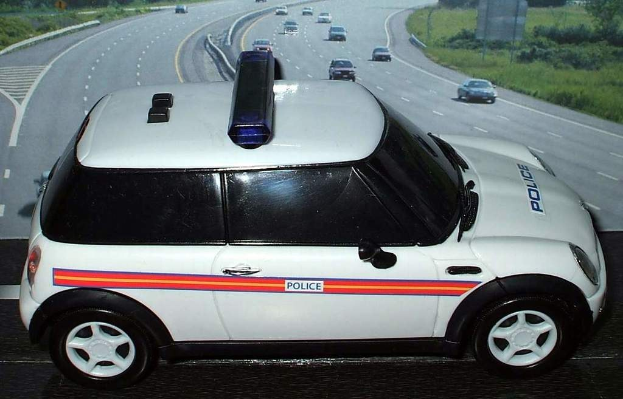 Weißer Polizeiwagen mit "Polizei" Aufschrift auf einer Straße außerhalb der Stadt, umgeben von fließendem Verkehr und grasigen Bereichen mit Bäumen auf beiden Seiten.