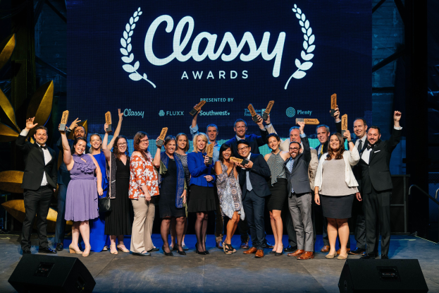 Gruppe von Menschen auf einer Bühne mit Auszeichnungen, unten Lautsprecher und einem Bildschirm mit "Classy Awards 2019" im Hintergrund.