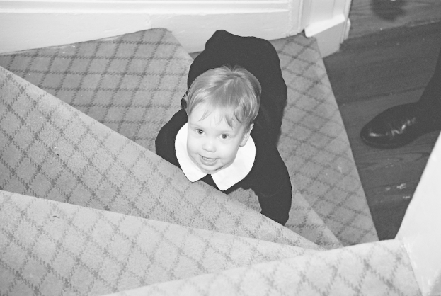 Ein Kind sitzt auf einer Treppe mit Schuhen, die rechts platziert sind, auf einem Schwarz-Weiß-Bild.