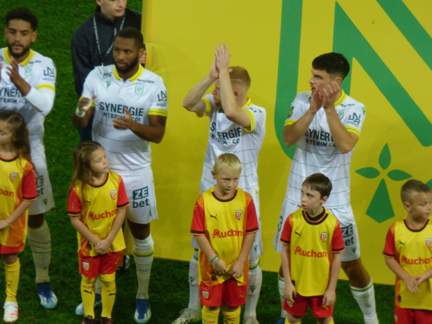Eine Gruppe von Fußballspielern in Uniformen, die feierlich klatschen, auf einem Ligue-1-Feld mit einem "Ligue 1"-Schild im Hintergrund.
