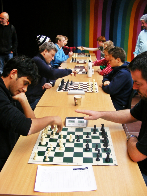 Zwei Personen sitzen sich gegenüber und spielen Schach mit einem Timer auf dem Tisch.