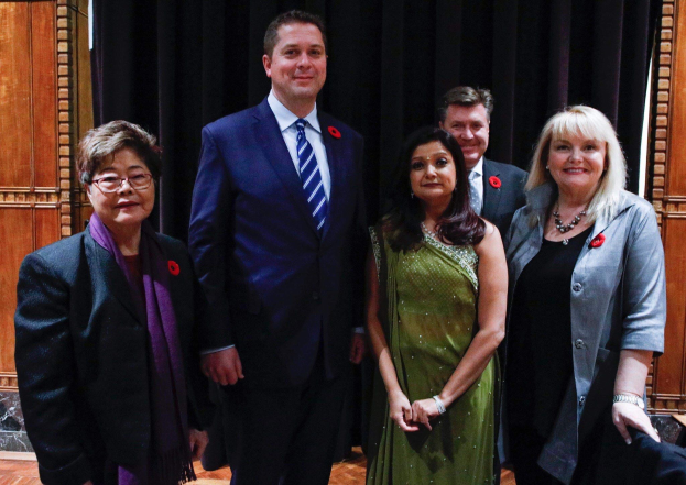 Gruppe von Menschen vor schwarzem Vorhang mit Holzwand im Hintergrund, die scheinbar Liberale bei einer Versammlung sind.