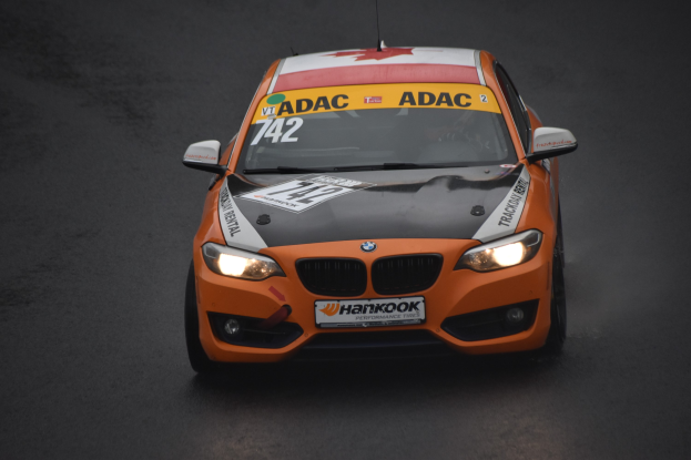 Ein oranges BMW-Rennfahrzeug mit Text und Zahlen darauf, das auf einer Rennstrecke fährt.