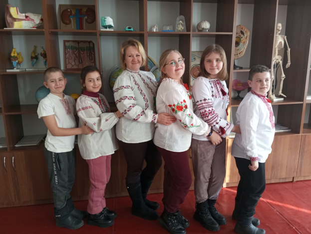 Eine Gruppe von Kindern in traditioneller ukrainischer Kleidung vor einem Bücherregal mit Spielzeugen, einem Skelett und anderen Gegenständen.