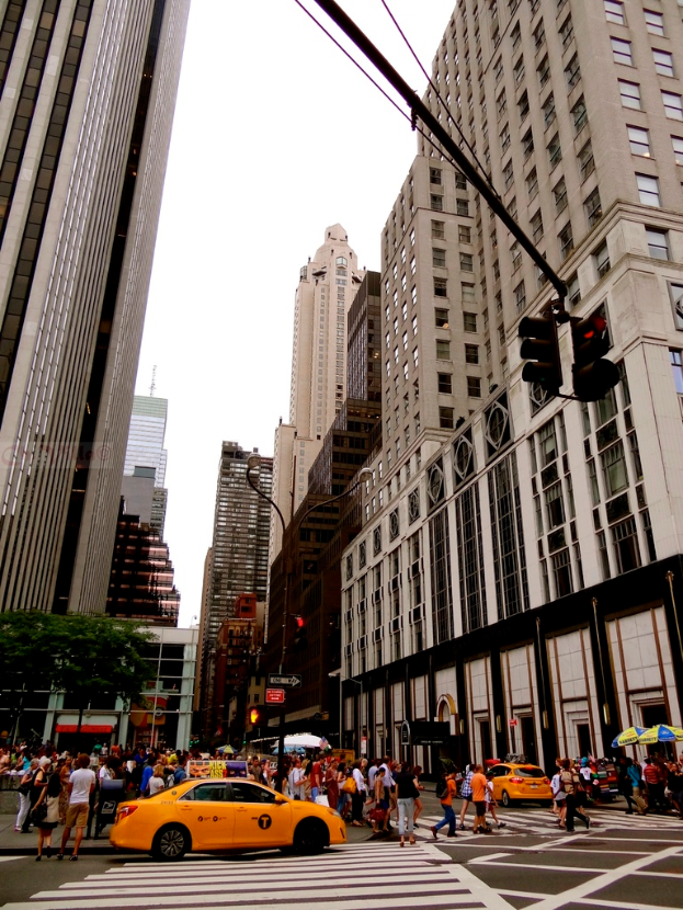Eine Stadtstraßenszene mit Gebäuden, Verkehrsampeln, Fenstern, einigen Fußgängern, Autos und Himmel.