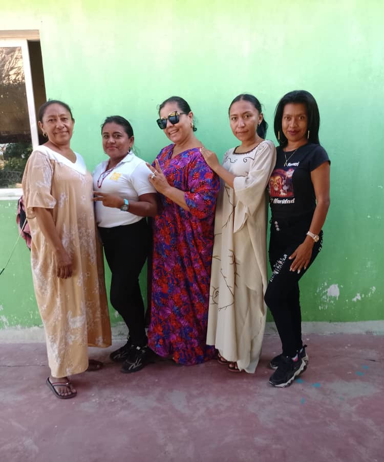 Eine Gruppe von Frauen, die vor einer grünen Wand mit einem Fenster auf der linken Seite stehen und an einem International Women's Day Event teilnehmen.