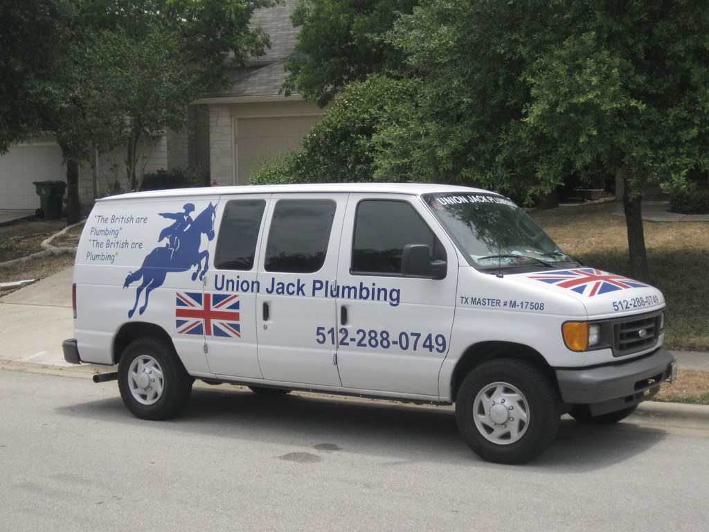 Ein Van auf der Straße mit einer Flaggengestaltung und Text auf der Seite, mit einem Haus und Bäumen im Hintergrund.