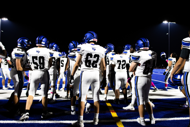 Eine Gruppe von Fussballspielern in Helmen und Stiefeln steht auf einem Feld, mit Leuchten im Hintergrund.