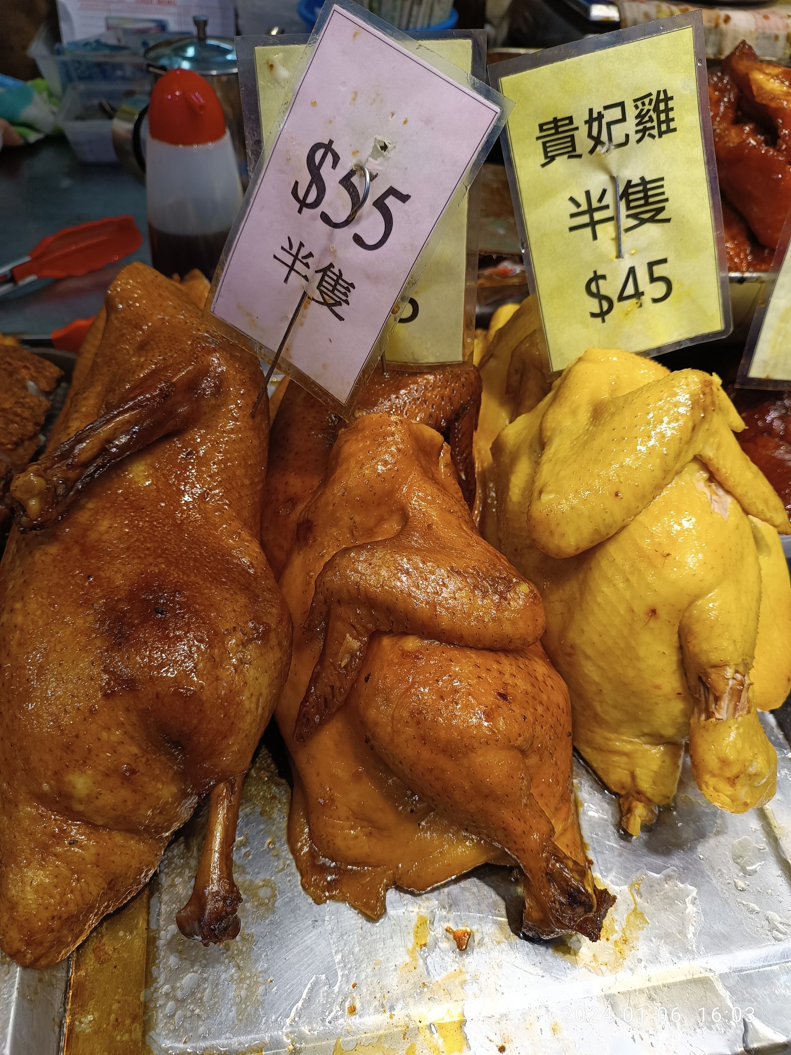 Eine Ansammlung von Hühner auf einem Metalltablett mit Preisschildern in einem belebten Markt.