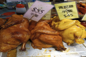 Eine Ansammlung von Hühner auf einem Metalltablett mit Preisschildern in einem belebten Markt.