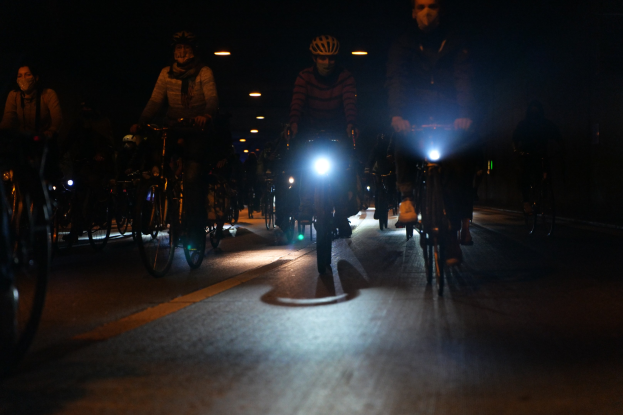 Eine Gruppe von Menschen, die nachts mit Fahrrädern auf einer Straße fahren, alle tragen Helme.
