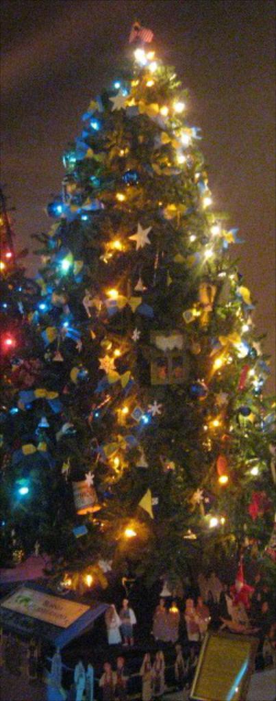 Ein geschmückter Weihnachtsbaum mit Statuen von Menschen auf einem darunter platzierten Tisch.