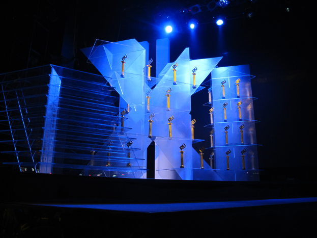 Eine Bühne für eine Preisverleihung mit dunklem Hintergrund, beleuchtet von ein paar Lichtern und mit mehreren Gegenständen, die sich auf das Ereignis beziehen.