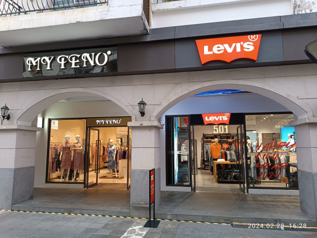 Storefront of Levi's clothing brand with mannequins in dresses, hanging clothes, and illuminated displays above a road.