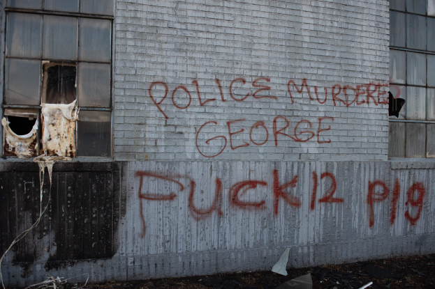 Ein Gebäude mit Graffiti, das "Polizei Mord George Fuck 12 P19" auf der Seite trägt und Fenster sowie verschiedene Gegenstände vor sich hat.