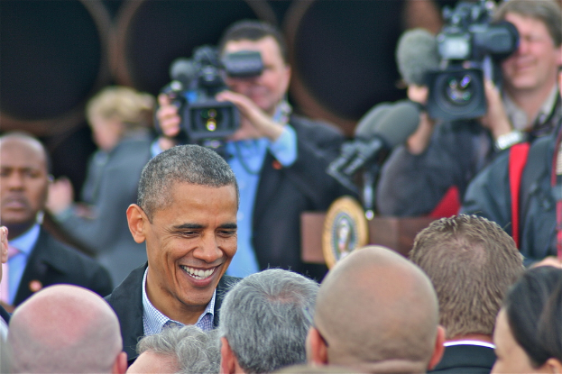 Ein Mann steht in der Mitte und spricht zu einer Gruppe von Menschen vor ihm, während zwei Personen im Hintergrund die Szene mit Kameras aufnehmen.