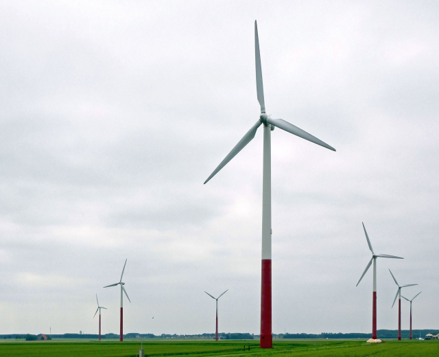 Eine Gruppe hoher, weißer Windkraftanlagen in einem grünen Feld mit Bäumen und Wolken im Hintergrund.