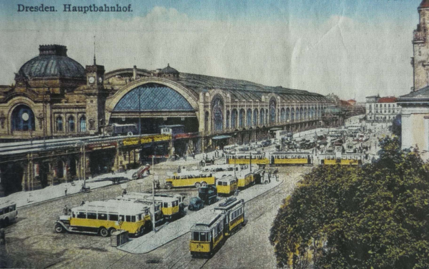 Eine alte Postkarte zeigt den Dresden Hauptbahnhof in Dresden, Deutschland, mit einer belebten Straßenszene, Fußgängern, Bäumen, Gebäuden und einem bewölkten Himmel.