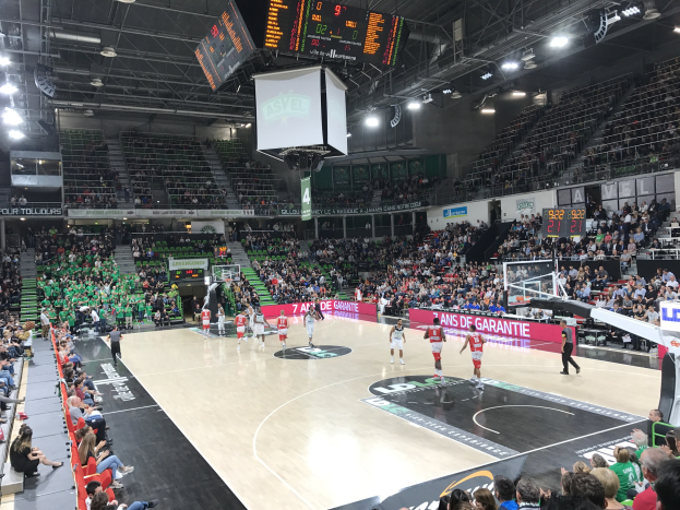 Basketballspiel in einer großen Arena mit Zuschauern, mit Teams Asvel und Galatasaray, wie es auf den Werbetafeln am Spielfeldrand zu sehen ist.