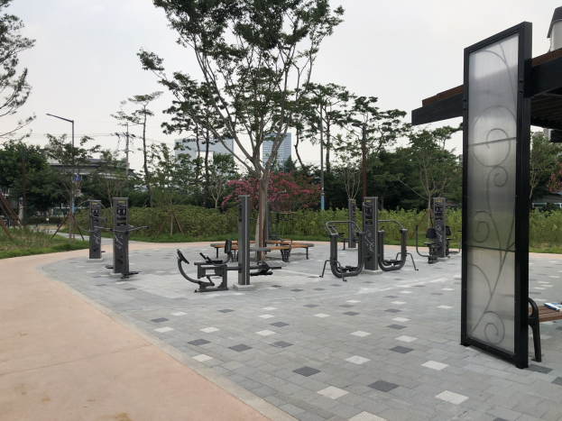 Outdoor park featuring various fitness equipment, greenery, and urban elements under a sky backdrop.