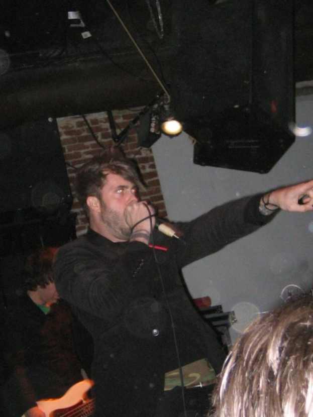 Eine Gruppe von Menschen mit einem Mann, der in ein Mikrofon singt, in der Mitte, mit Lichtern im Hintergrund.