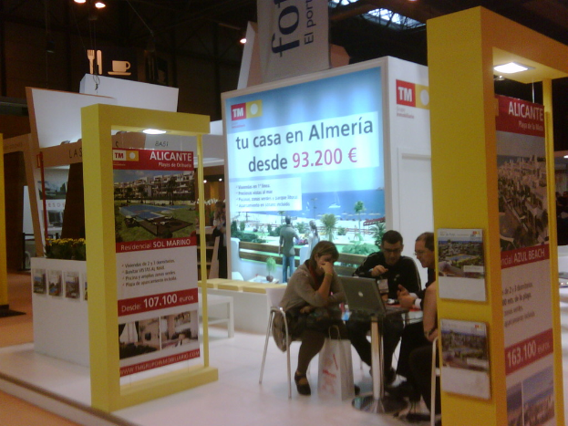 Eine Gruppe von Menschen sitzt um einen Tisch herum und schaut auf einen Laptop, mit mehreren Flyern mit verschiedenen Werbeanzeigen daneben.