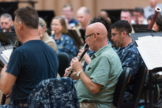 Eine Gruppe von Männern, die Klarinetten spielen, in einem Raum mit Bücherständern vor ihnen, was darauf hindeutet, dass sie Teil einer Band sind.