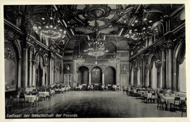 Schwarz-weiß-Fotografie eines großen Saals mit Tischen, Stühlen, Säulen, Bögen und Kronleuchtern, beschriftet mit 'Festival der Gesellschaft der Freunde, Berlin' unten.
