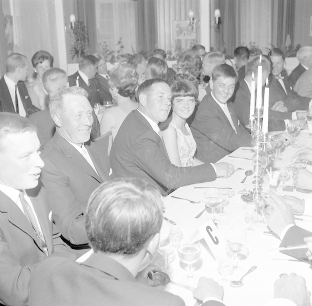 Eine Gruppe von Menschen sitzt um einen langen Tisch mit Essbesteck, Kerzen und warmem Licht im Hintergrund.