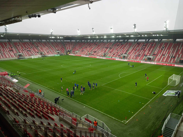 Ein Fußballfeld in einem Stadion mit Zuschauern rundherum unter Stadionbeleuchtung, mit dem Himmel im Hintergrund.