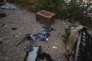 Müllhaufen mit einem Plastikbehälter und Kleidung, die auf dem Boden neben einem Zaun verstreut sind.