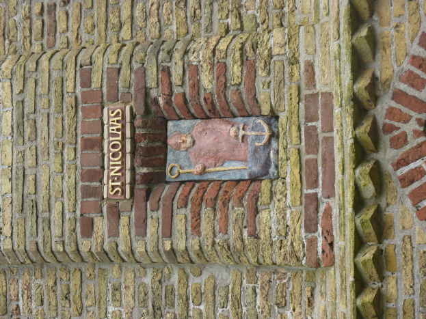 Eine Backsteinwand mit einer Steinplatte, auf der in fetter Schrift 'Heiliger Nikolaus' steht.