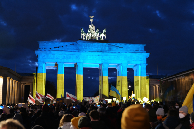 Eine Menschenmenge steht vor dem Brandenburger Tor in Berlin, Deutschland, mit Fahnen und Plakaten in den Händen, mit einer Banner auf der rechten Seite.