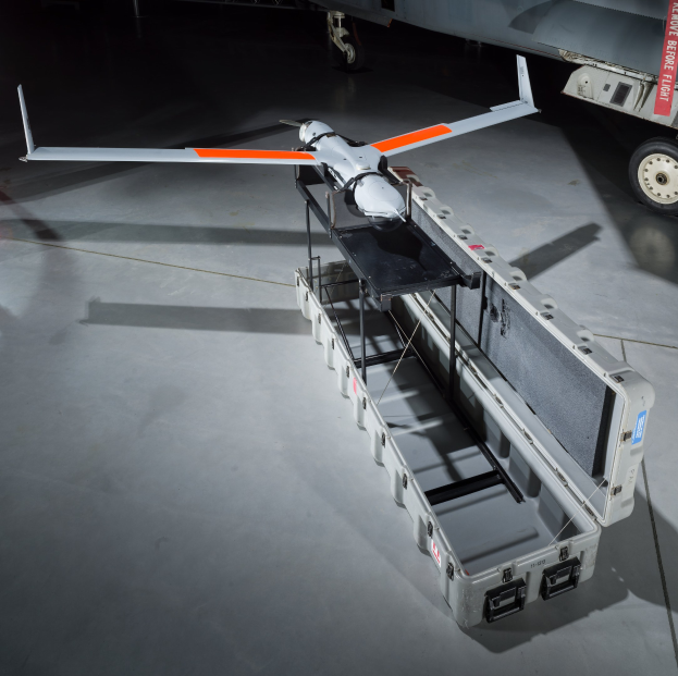 Ein graues MQ-9 Reaper-UAV in einer Hangar, mit einer Kiste auf dem Boden und einem Fahrzeug auf der rechten Seite.