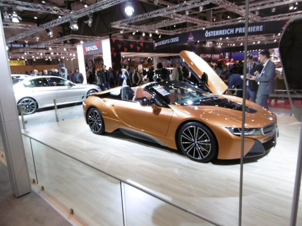 Ein stylischer schwarzer BMW i8 Roadster mit Chromakzenten auf der Frankfurt Motor Show umgeben von formell gekleideten G├Ąsten in einer Atmosph├Ąre der Aufregung.