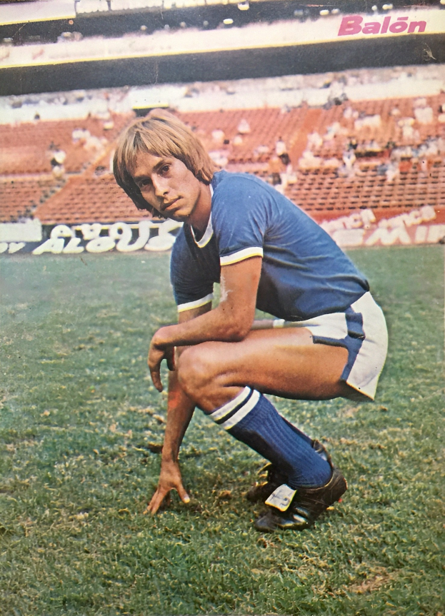 Ein Mann kniet auf einem Fußballfeld umgeben von Menschen, die auf Stühlen und Tafeln mit Text sitzen.