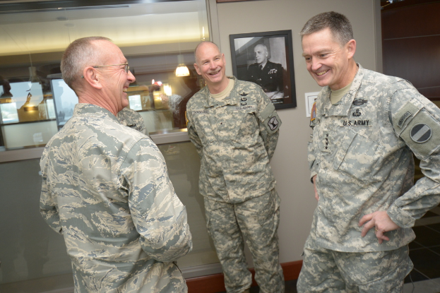 Drei uniformierte Männer, die vor einer Wand mit einem Foto-Rahmen, einem Glasfenster mit Laternen und Tischen und einer braunen Tür auf der rechten Seite stehen und lächeln.