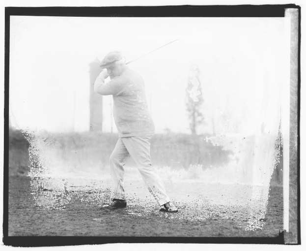 Altes Schwarz-Weiß-Foto eines Mannes beim Golfschlagen auf dem Gelände mit Pflanzen und Bäumen im Hintergrund.