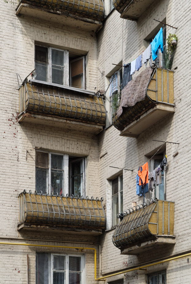 Ein Wohnhaus mit Fenstern, Balkonen, Wäsche, die zum Trocknen aufgehängt ist, und Rohren an der Seite.