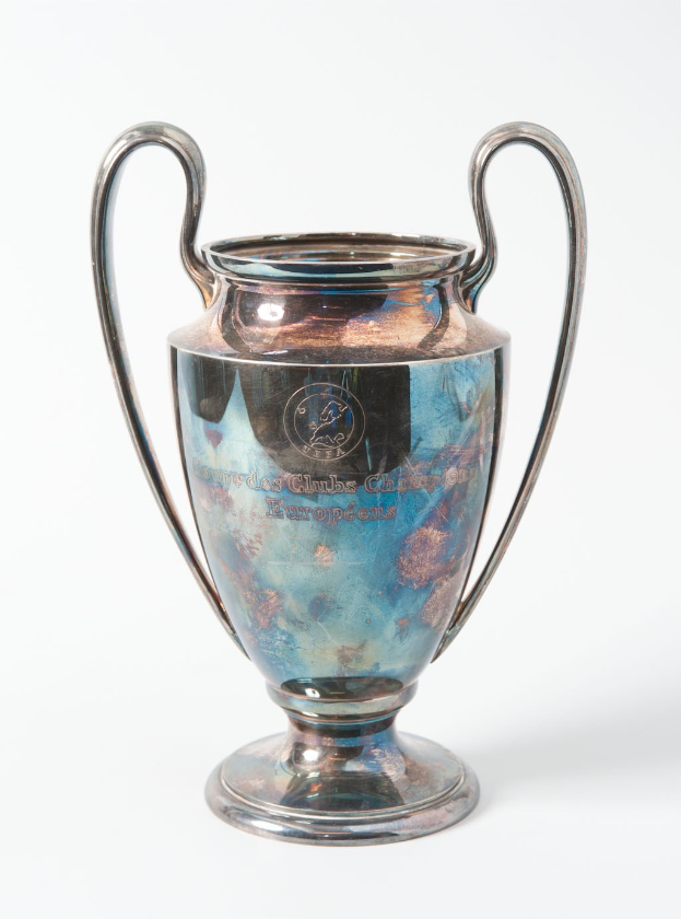 Der UEFA-Champions-League-Pokal, ein stählerner Becher mit zwei Griffen und einem blauen und silbernen Farbschema, der mit «UEFA Champions League» beschriftet ist, vor einem weißen Hintergrund dargestellt.