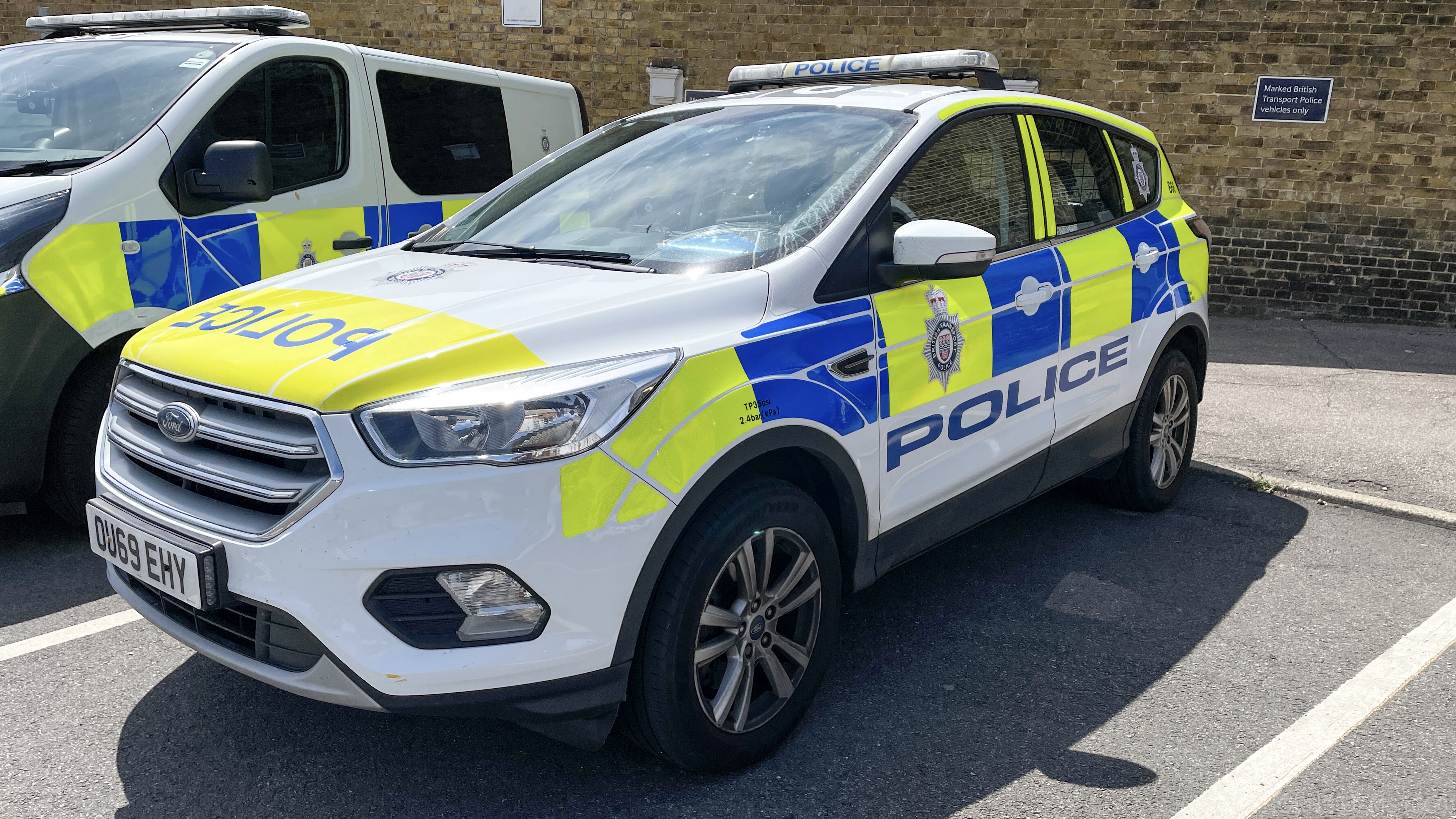 Zwei Polizeiwagen nebeneinander auf einem Parkplatz geparkt, mit einer Wand und einem Textschild im Hintergrund.