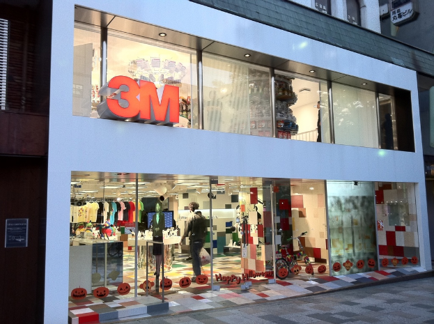 Ein Gebäude mit einer Glaswand, auf der Kleider an Bügeln, eine Schaufensterpuppe, ein Fahrrad, aufgeklebte Bilder und Schrift auf der Glaswand zu sehen sind.