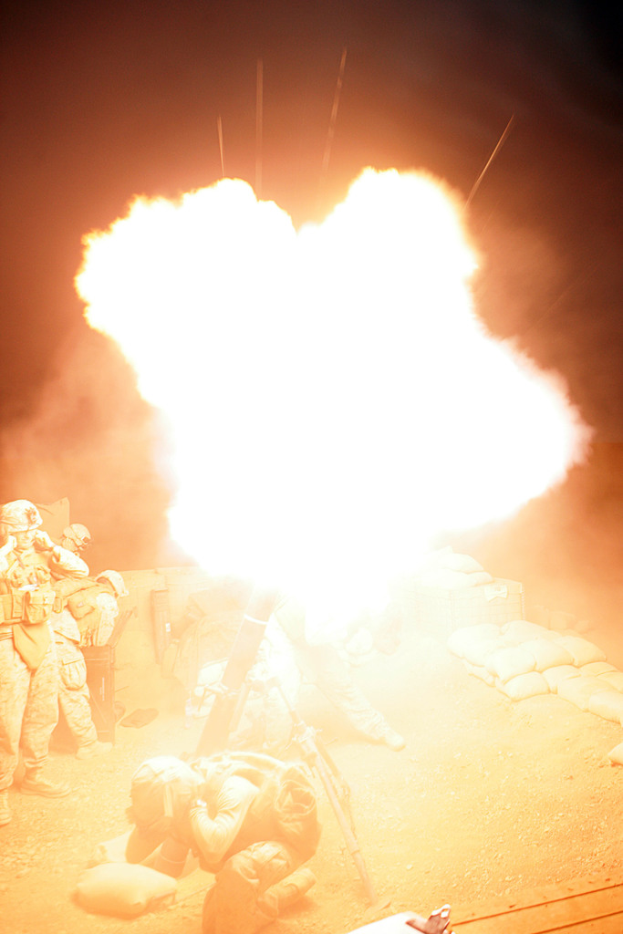 Mehrere Personen in Uniformen und Helmen befinden sich auf einem Gelände mit einigen Taschen, die herumliegen, und ein Feuer brennt in der Mitte der Szene.