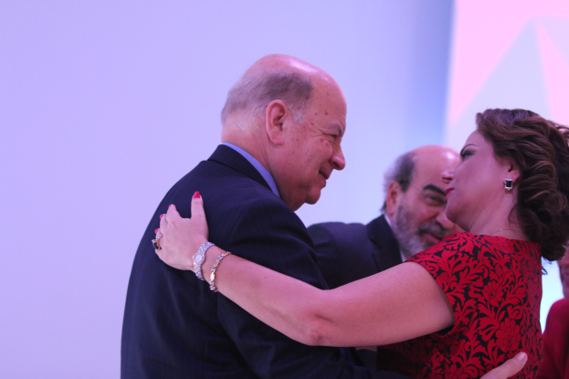 Ein Mann und eine Frau umarmen sich herzlich auf einer Bühne, umgeben von ein paar anderen Menschen, wobei der Mann ein Armband trägt.