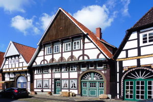 Reihe von Fachwerkhäusern in Heidelbergs Altstadt mit Fahrzeugen auf der Straße und bewölktem Himmel.