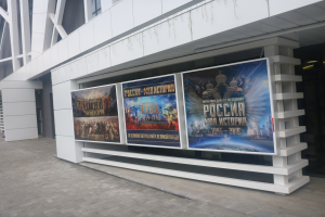 Großes Plakat an einem Gebäude, das die Eröffnungszeremonie der Olympischen Spiele in Moskau ankündigt, mit beleuchteten Seiten und sichtbarem Boden.