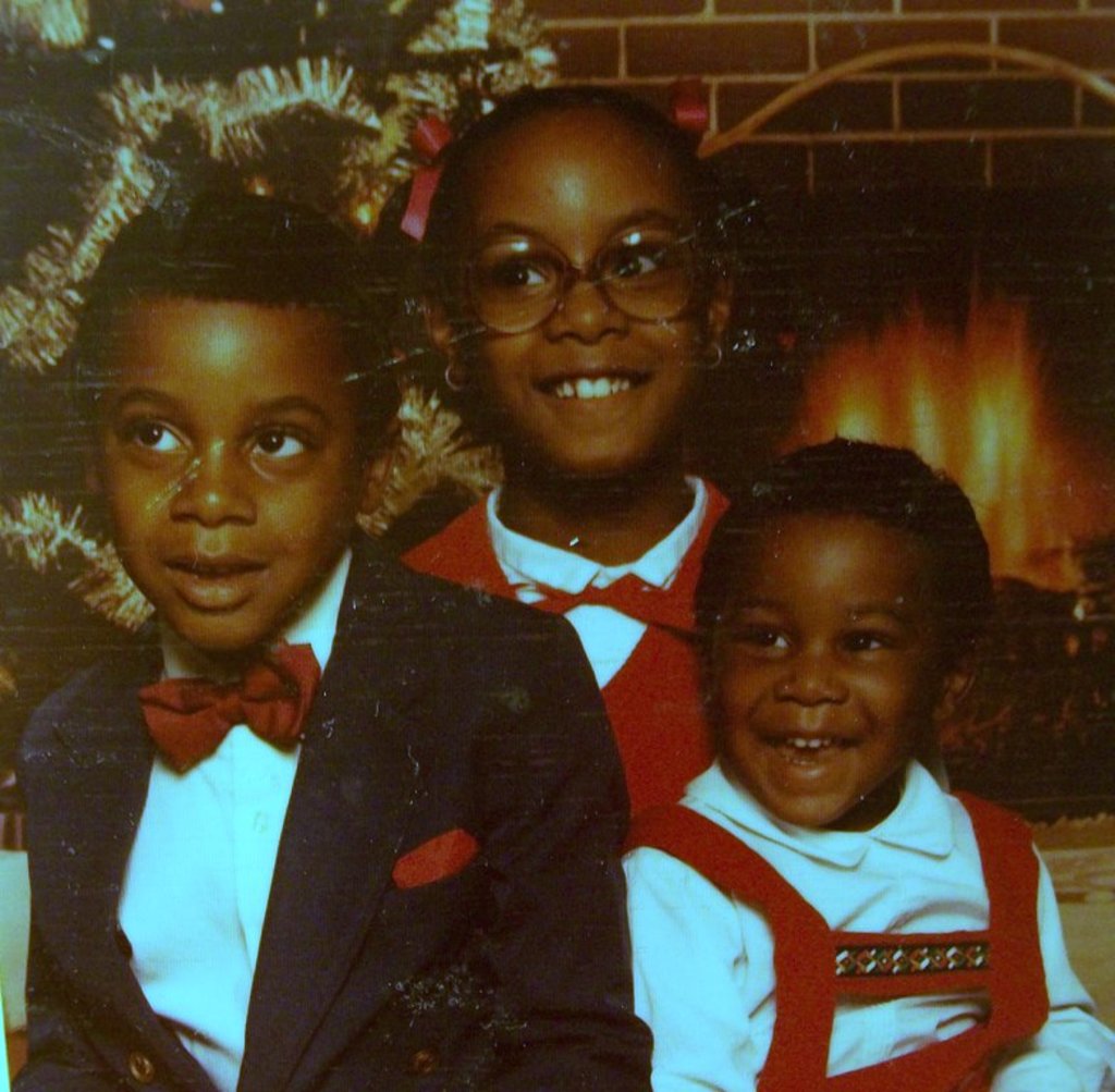 Drei Kinder, die vor einem Weihnachtsbaum mit einem Kamin aus Holz lachen.