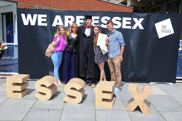 Eine Gruppe von Menschen, die strahlen und lächeln, halten ein Zertifikat, mit einem Gebäude und einem Netz im Hintergrund.