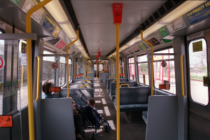 Innenseite eines öffentlichen Verkehrsmittels mit Sitzreihen, einem offenen Fenster und einem Baby im Kinderwagen, mit sichtbaren Hinweistafeln.